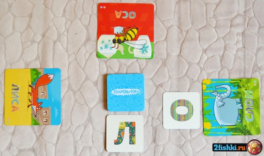 У трёх игроков по карте с картинками: оса, слон и лиса. По центру стопка карт с буквами рубашкой вверх. Из неё на стол выложены 2 карты с буквами "О" и "Л".